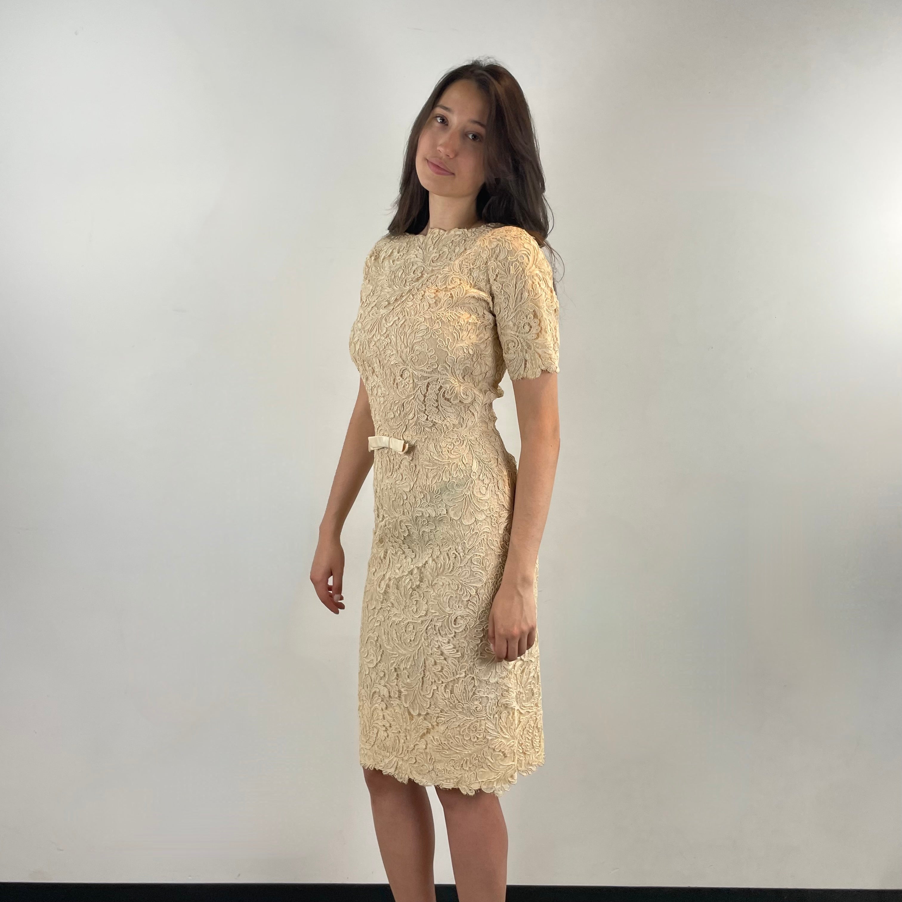 Boheme Vintage 1960s ivory lace dress with scalloped edges, dolman sleeves, and satin bow waist detail.