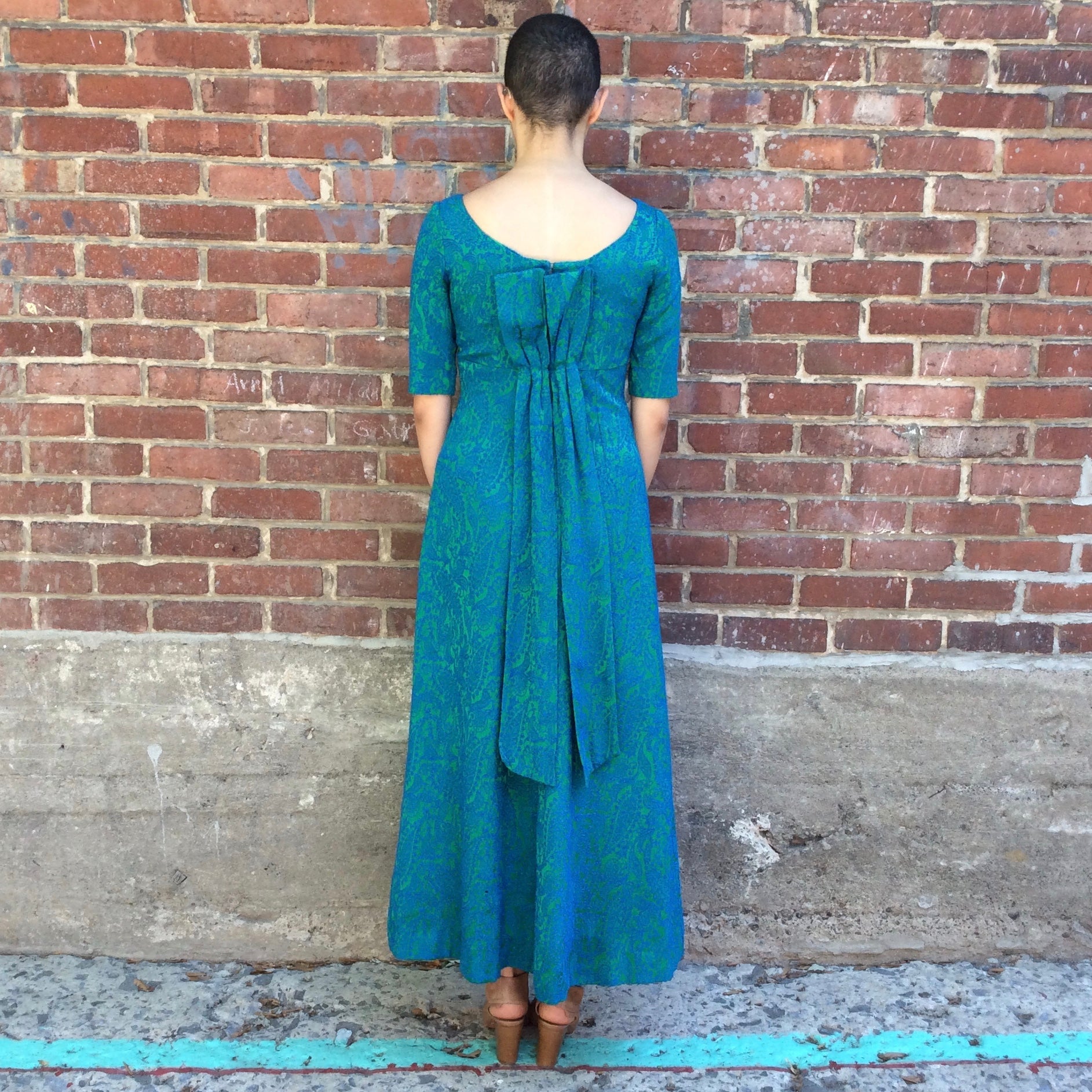 Back of Vintage 1960s blue and green brocade ankle-length evening dress with empire waist and low back detail, photographed in Montreal for Boheme Vintage – https://bohemevintage.com
– Montreal vintage fashion boutique.