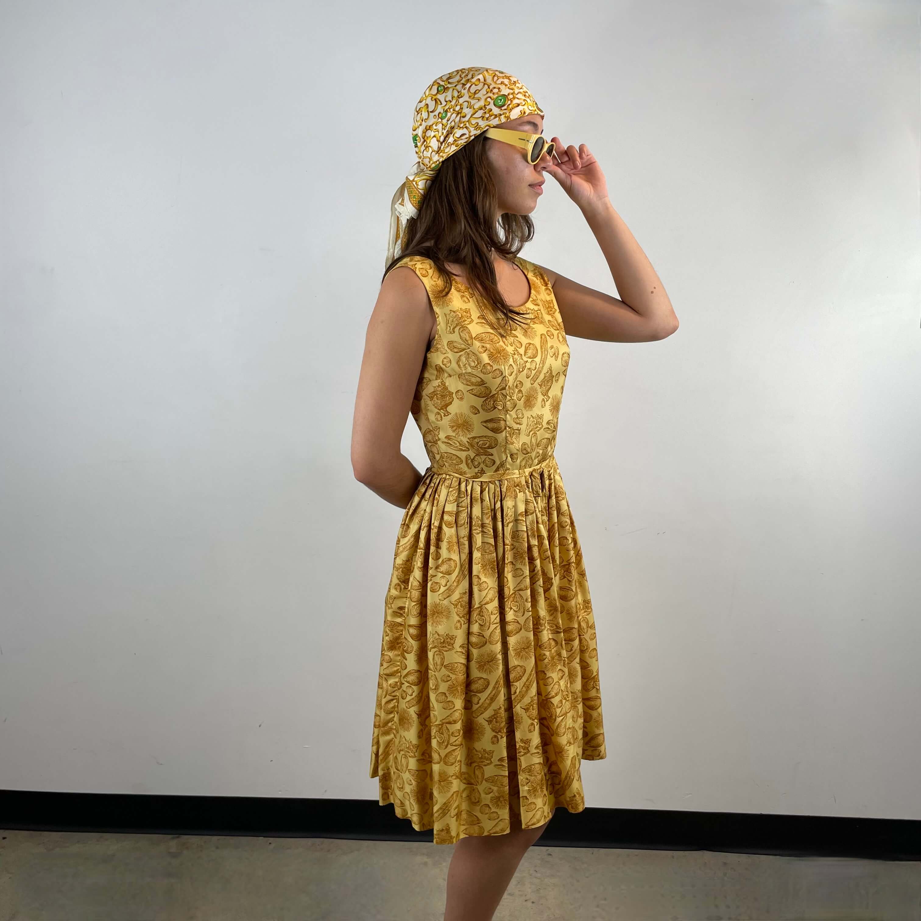 Side view of Boheme Vintage 1950s L’aiglon seashell print gold acetate dress with pleated skirt and fitted bodice.