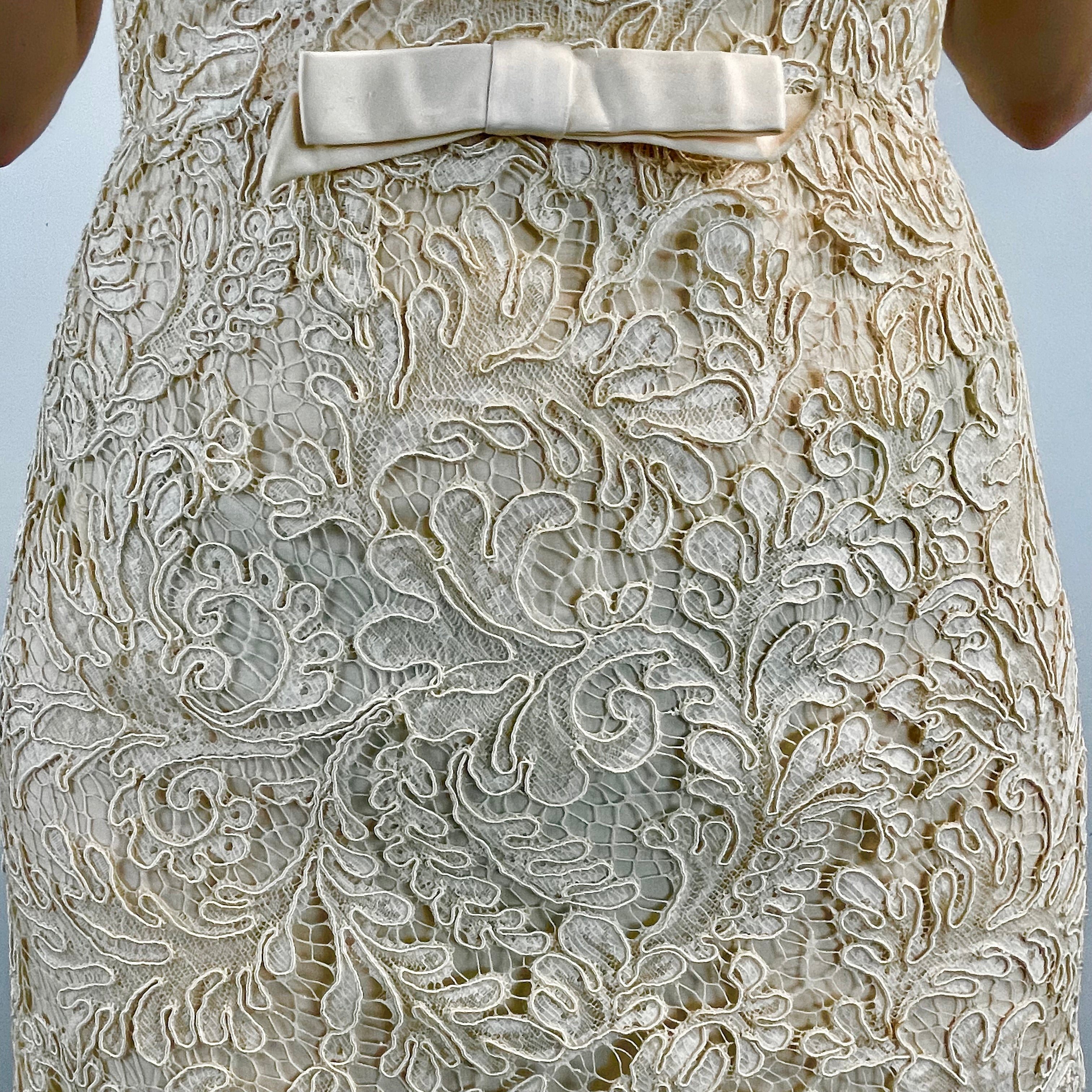 Close Up View of Boheme Vintage 1960s ivory lace dress with scalloped edges, dolman sleeves, and satin bow waist detail.